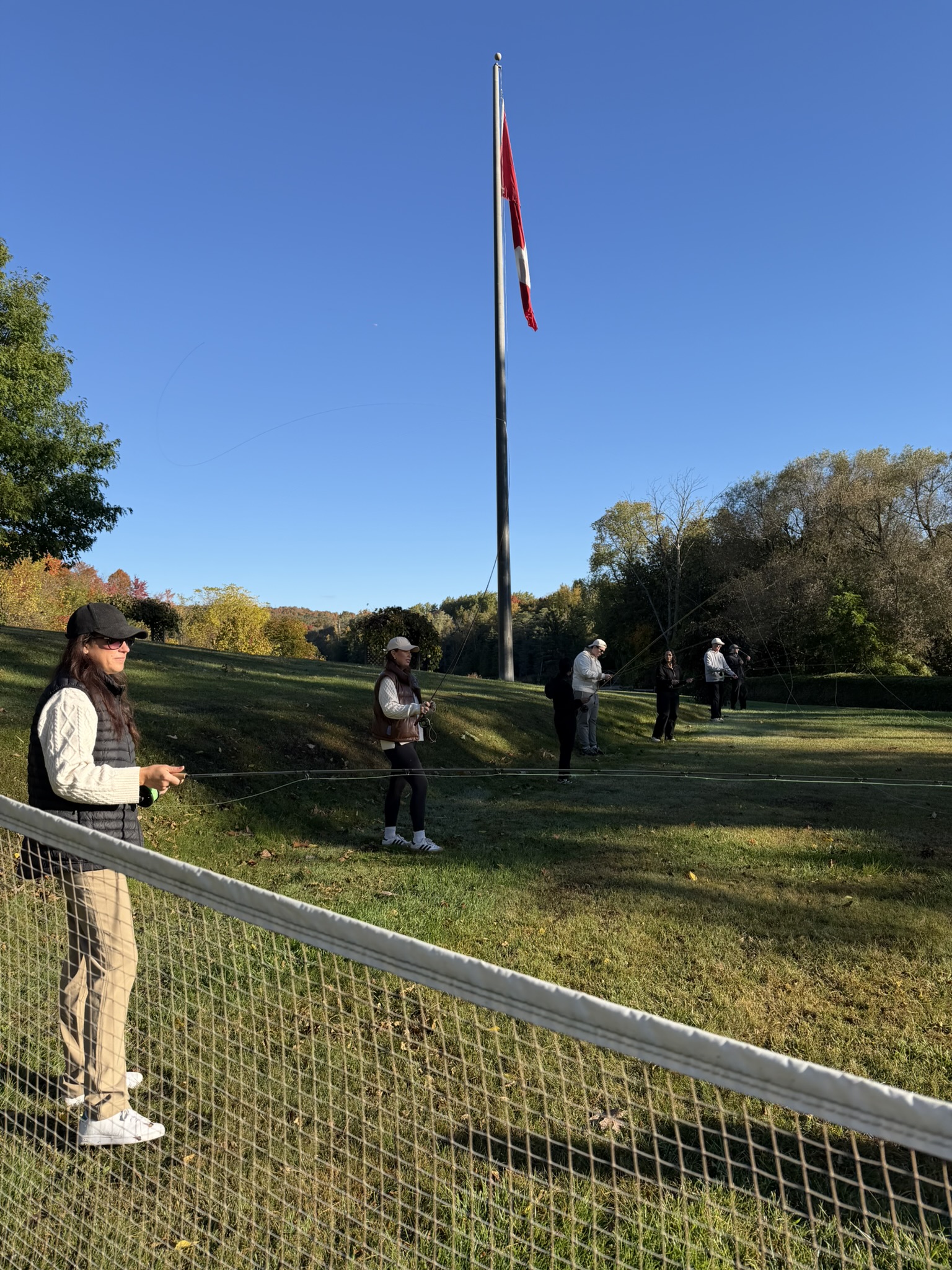 Participants practising fly fishing outdoors beneath a Canadian flag